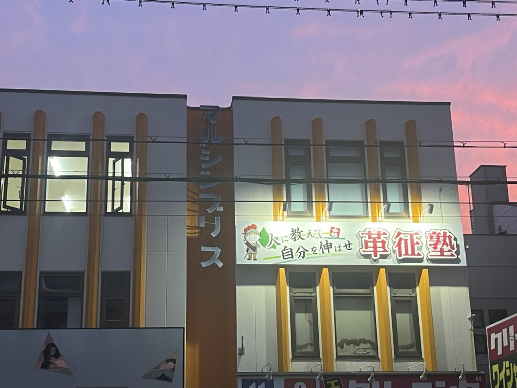 夕暮れに看板が灯る革征塾の外観